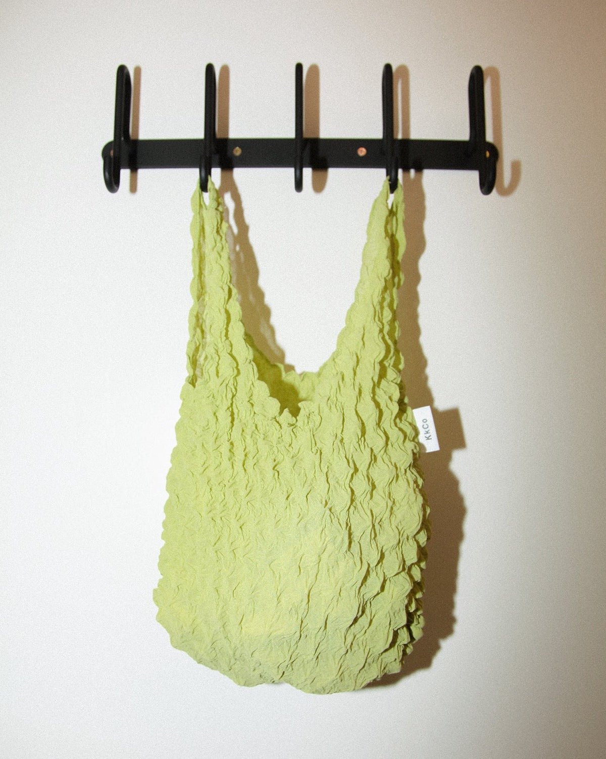 Small Bag in Popcorn Pleated Green Fabric by Kkco hanging from a wall mount coat rack 