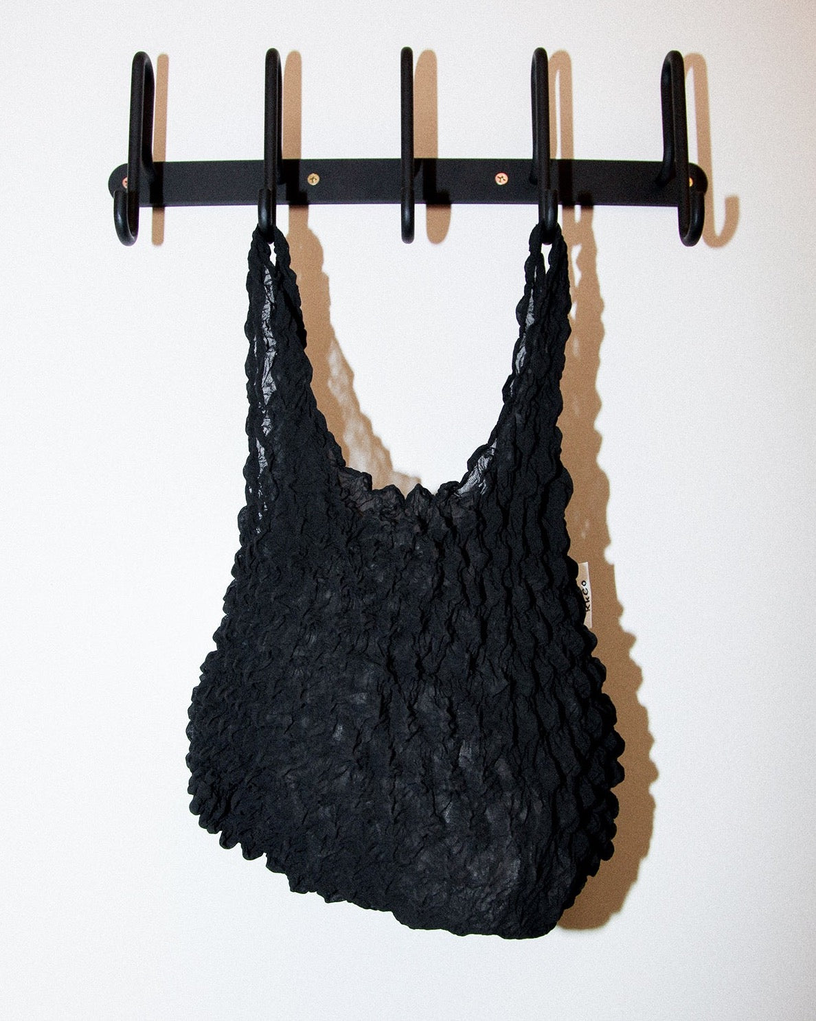 small handbag in a black popcorn pleated fabric from Kkco hanging from a wall mount coat rack