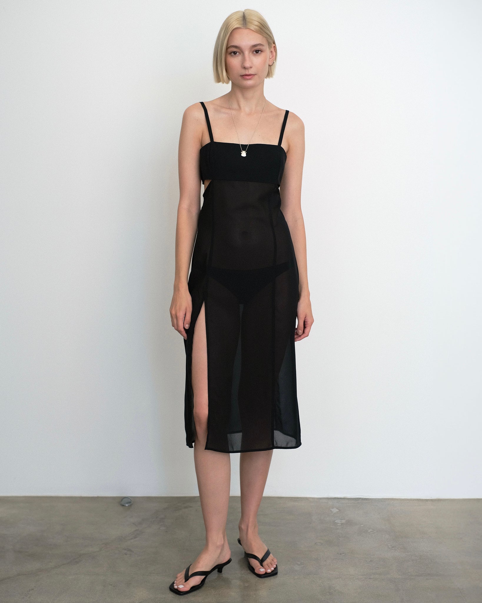 Model wearing a sheer, black midi dress with side slits from Una Hayde